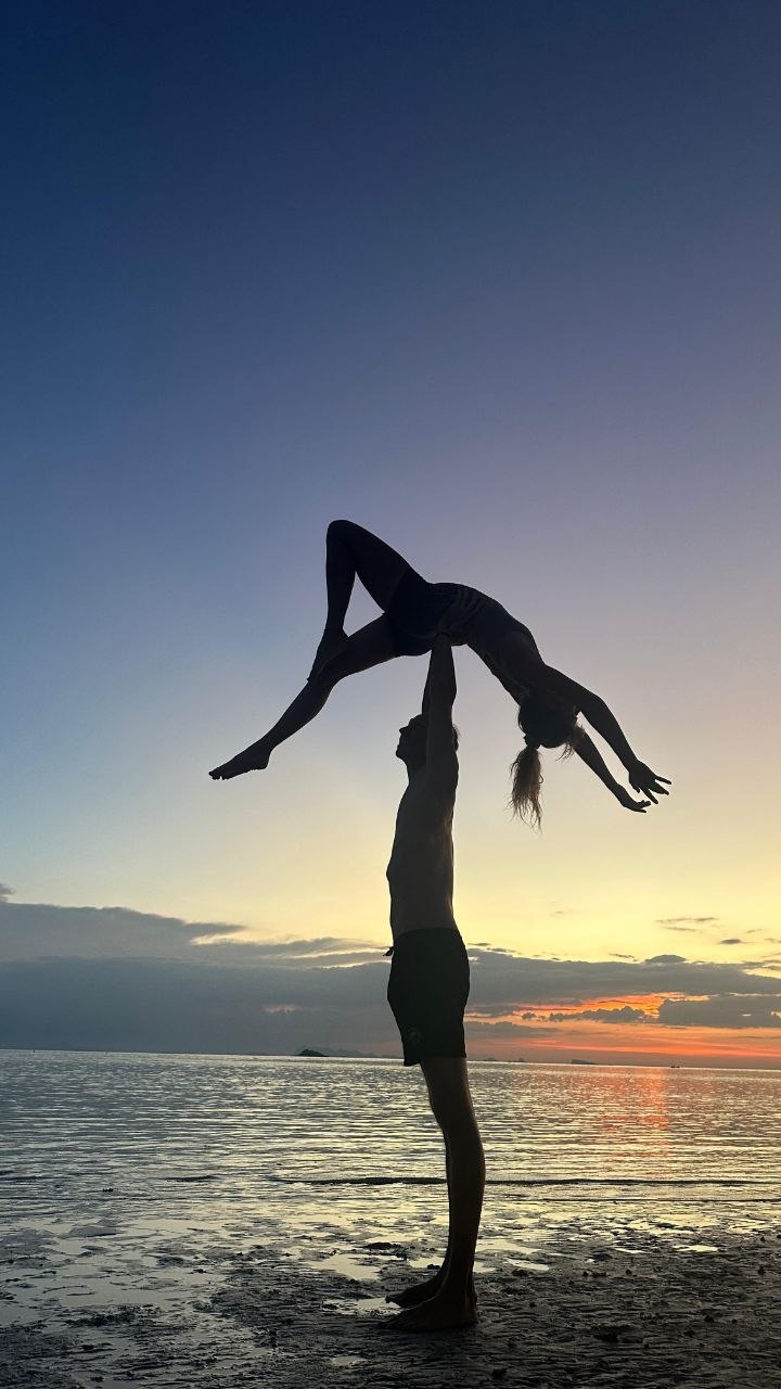 Silhouette of a one-arm partner lift on the beach at dusk