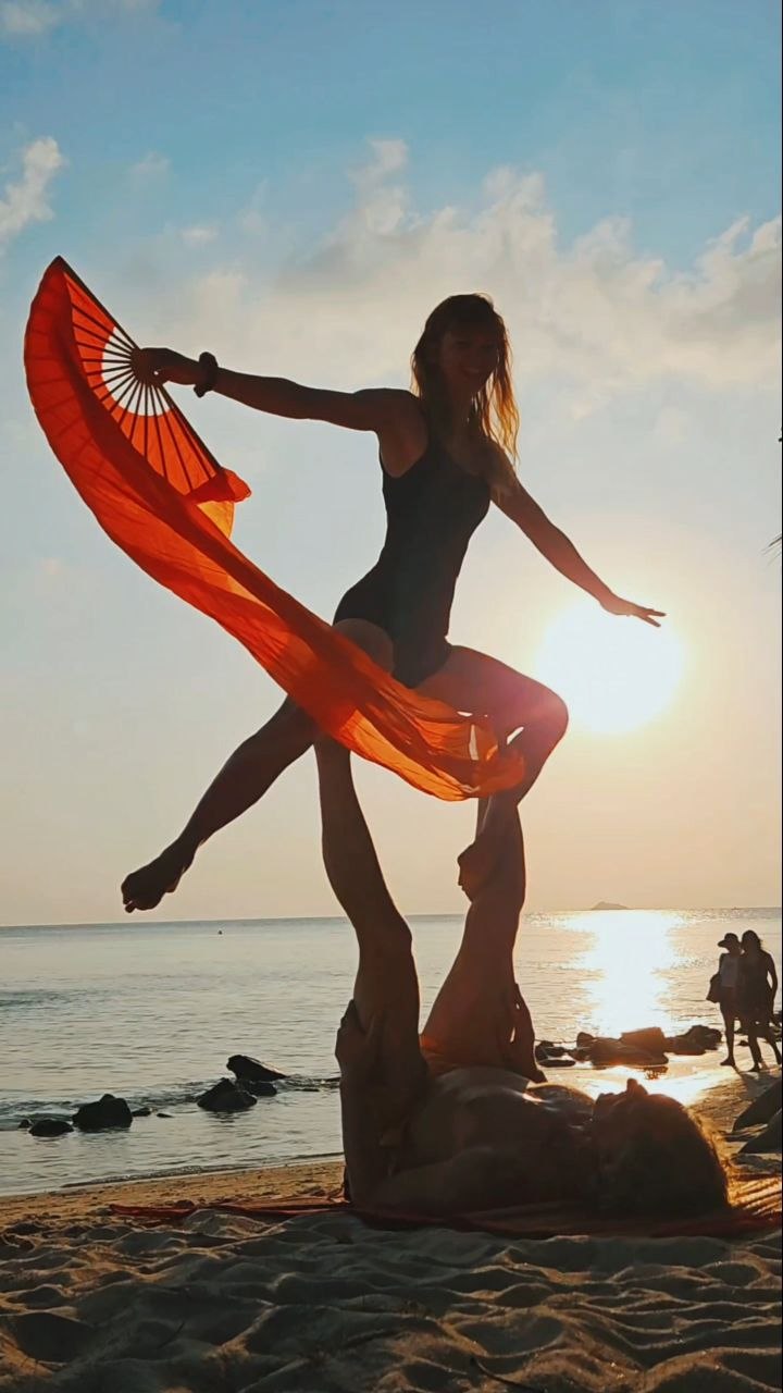 Partner acrobatics on the beach with a red silk fan