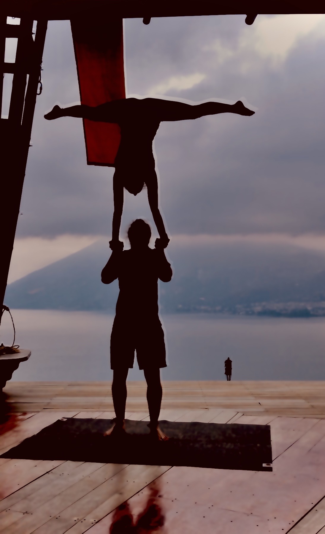 Silhouette of a hand-to-hand handstand in straddle above a lake